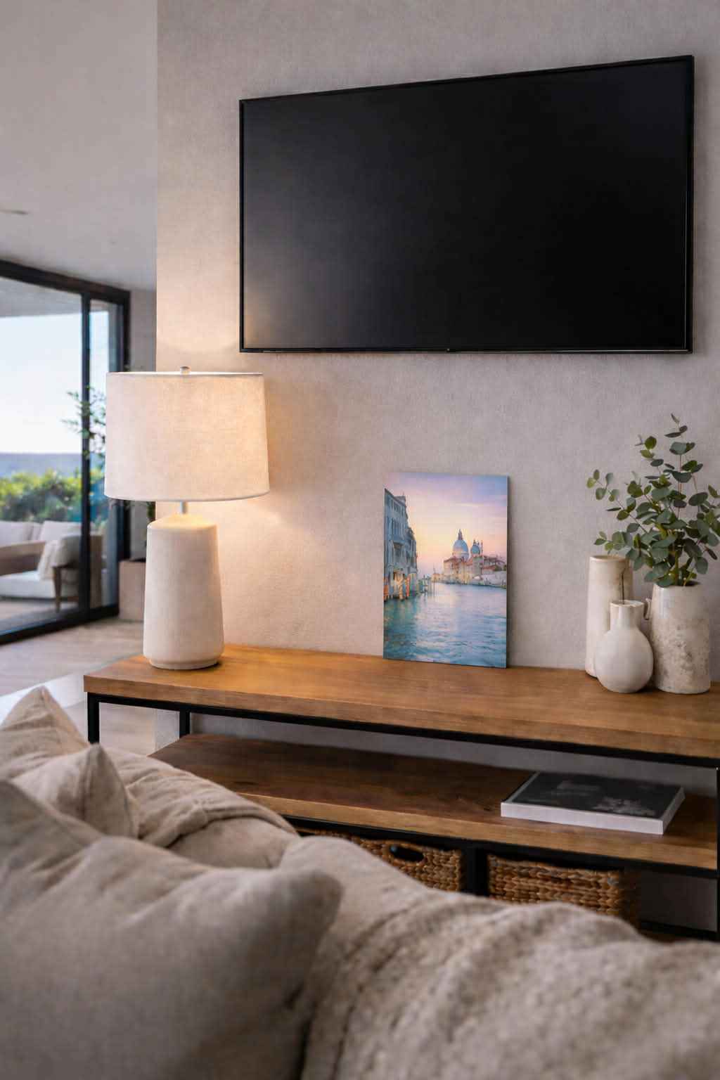 Modern living room with a TV, table lamp, decorative vases, and landscape wall art